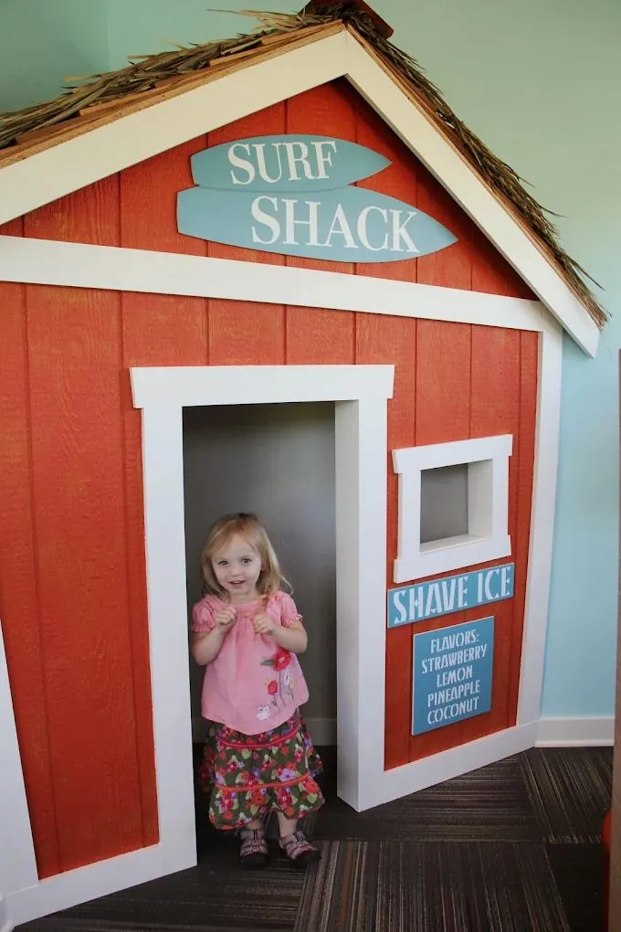 A smiling little girl standing in the doorway of the Surf Shack playhouse in our waiting room